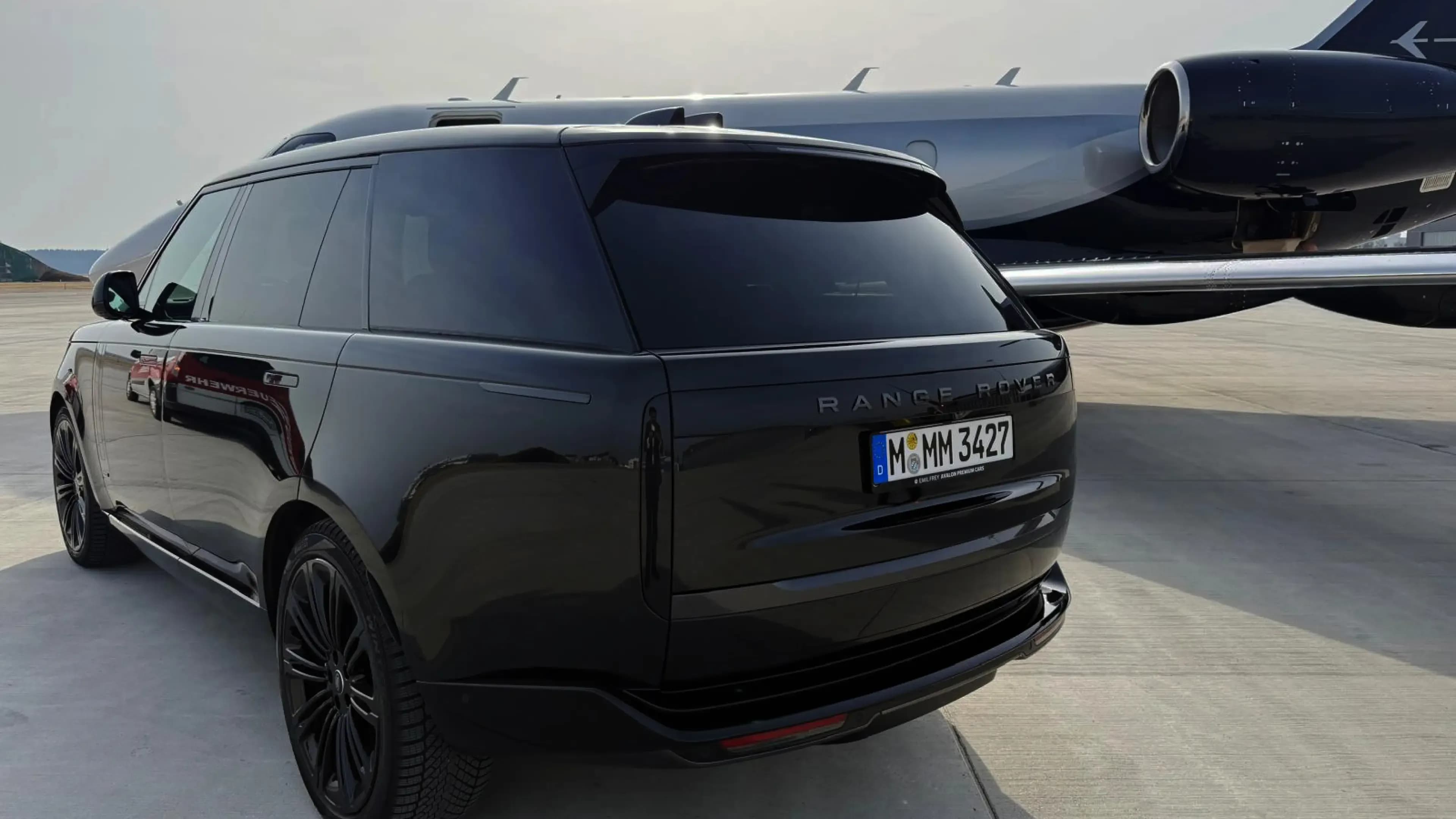 Range Rover Autobiography in Santorini Black rear view on airport apron beside a private jet – Mosaik Motors VIP airport transfer service Munich.