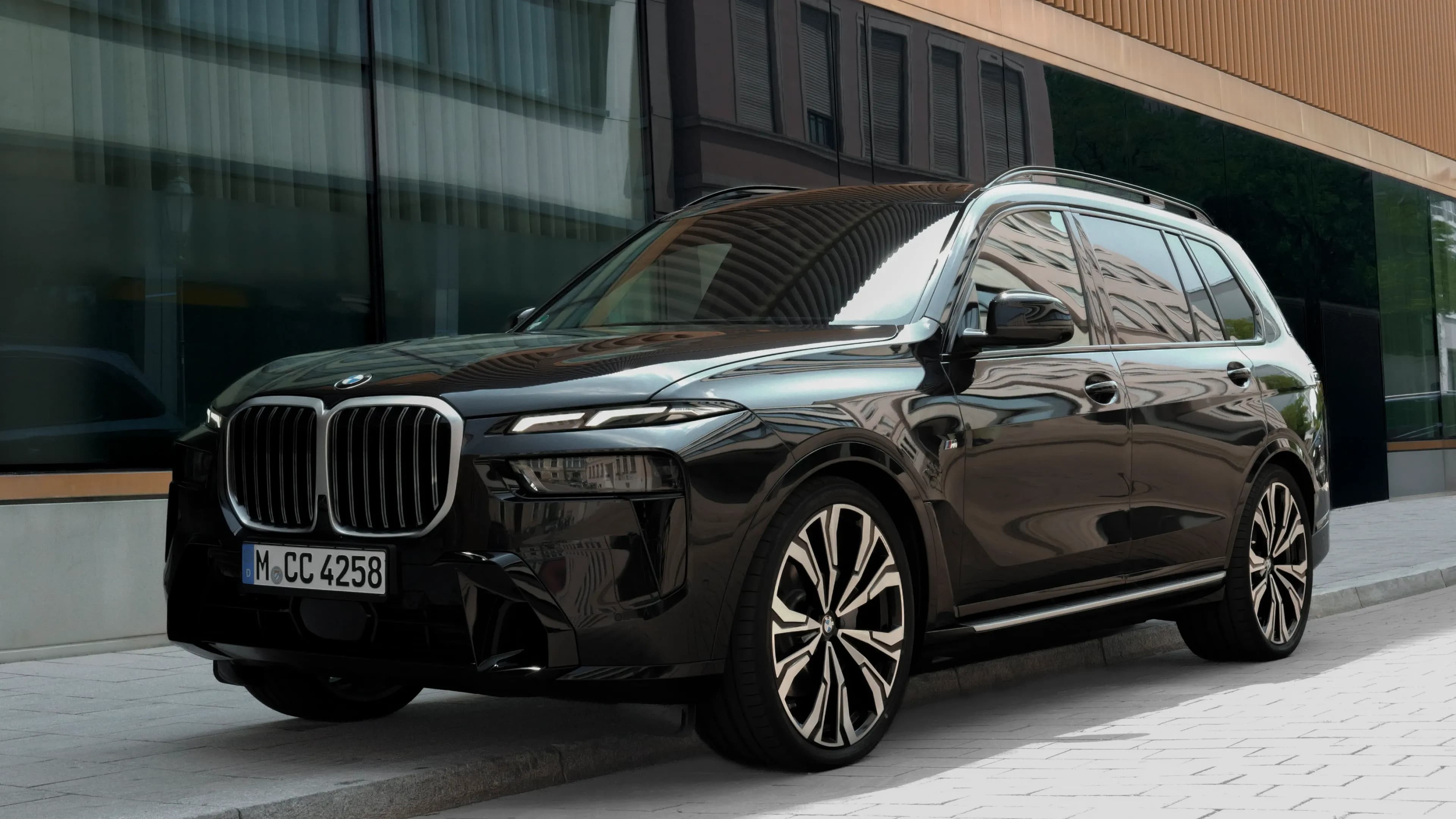 Black BMW X7 luxury SUV parked in front of the modern glass facade of the Lenbachhaus in Munich.