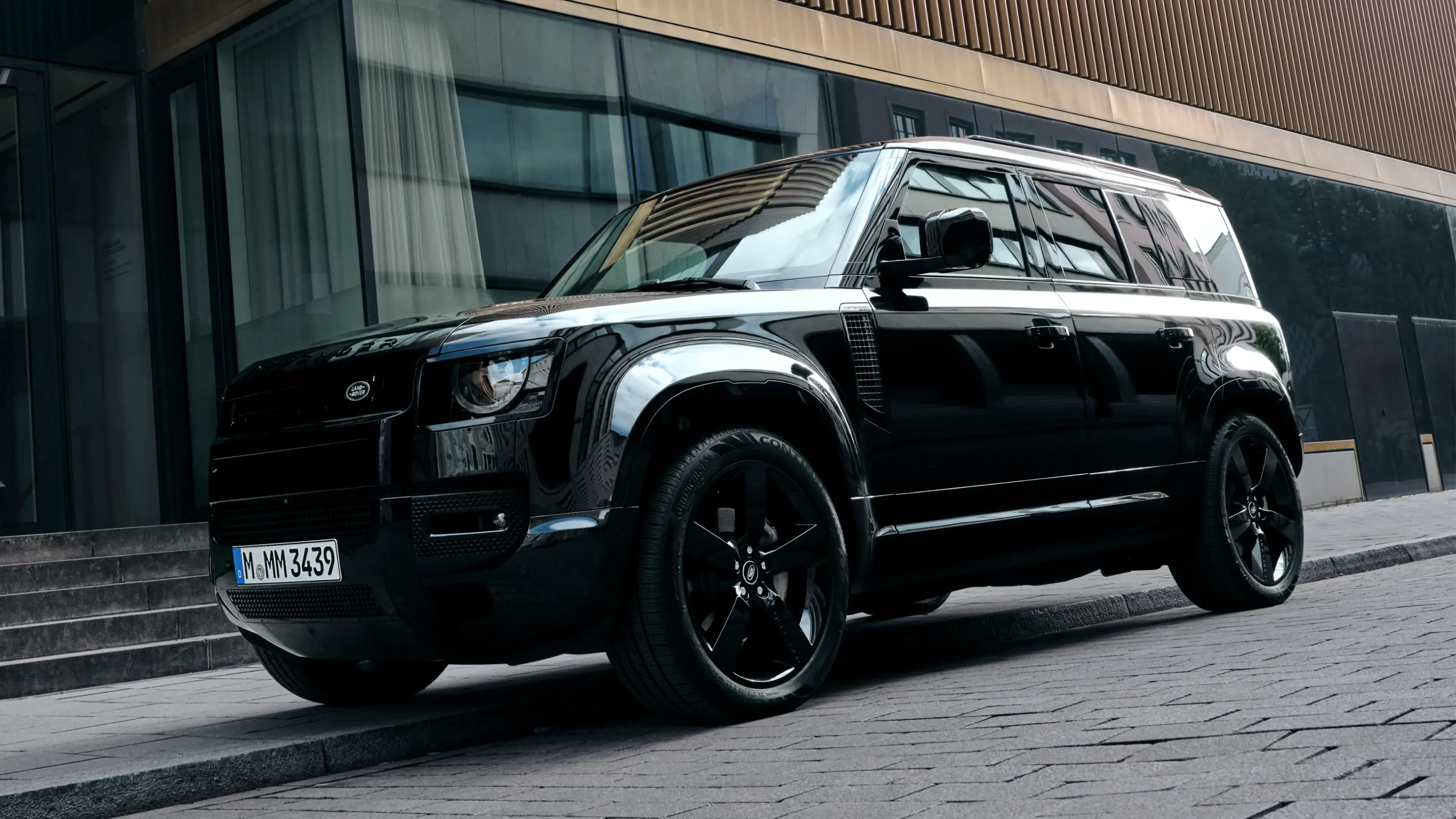 Black Land Rover Defender 90 in a front three-quarter view on a Munich cobblestone street, available for luxury car rental at Mosaik Motors