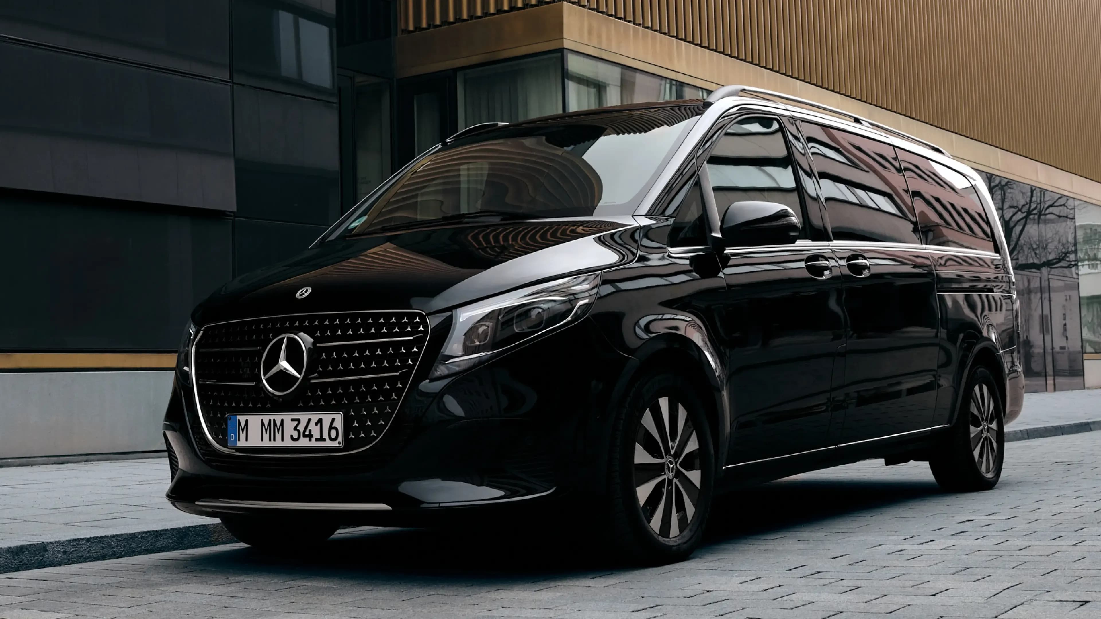 Black Mercedes-Benz V-Class luxury van from a front three-quarter view in front of the Lenbachhaus in Munich by Mosaik Motors, available for group travel and premium car rental at Mosaik Motors.