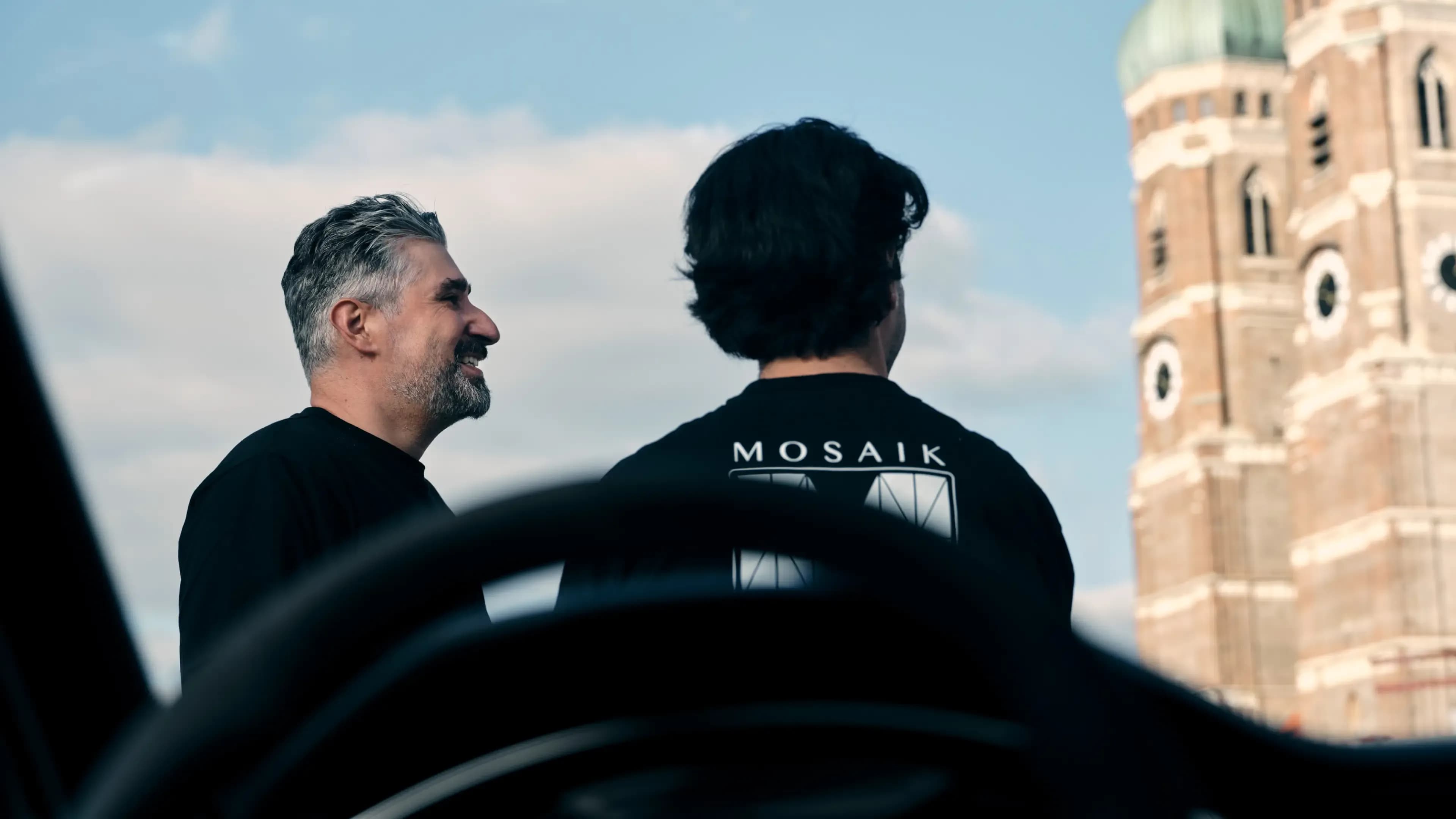 The founders of Mosaik Motors wearing Mosaik branded t-shirts in front of the Munich city skyline.